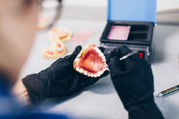 Dental prosthesis, prosthetics work. Close up of prosthetist hands while working on the denture. Selective focus.