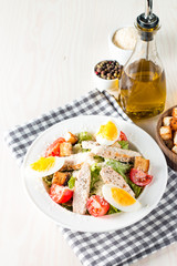 Fresh salad made of tomato, ruccola, chicken breast, eggs, arugula, crackers and spices. Caesar salad in a white, transparent bowl on wooden background