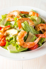 Fresh shrimp salad made of tomato, ruccola, avocado, prawns, chicken breast, arugula, crackers and spices. Caesar salad in a white, transparent bowl on wooden background