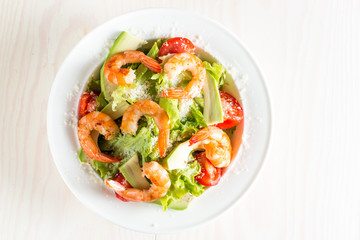 Fresh shrimp salad made of tomato, ruccola, avocado, prawns, chicken breast, arugula, crackers and spices. Caesar salad in a white, transparent bowl on wooden background
