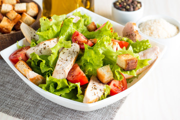 Fresh salad made of tomato, ruccola, chicken breast, eggs, arugula, crackers and spices. Caesar salad in a white, transparent bowl on wooden background