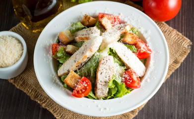 Fresh salad made of tomato, ruccola, chicken breast, eggs, arugula, crackers and spices. Caesar salad in a white, transparent bowl on wooden background