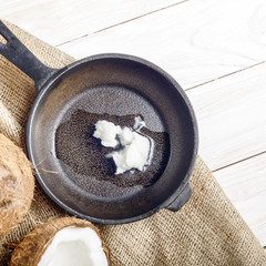 Coconut, shell with meat, cast iron skillet on hemp sackcloth on white wooden kitchen table