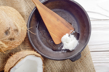 Coconut, shell with meat, cast iron skillet and spatula on hemp sackcloth on white wooden kitchen table
