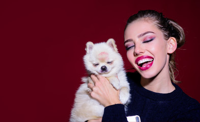 Sexy woman with little dog in her hand. Canine breed. Girl with bright makeup hugs her cute puppy. Lovely woman play with dog. Girl and puppy with eyes closed. Happy woman with Pomeranian spitz puppy.