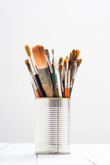 bunch of paint brush at tin can, on white wooden
