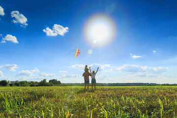 Mother, father and daughter are flying a kite in the field. Front view, copy space.