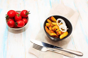 Home made potato food with tomatos cherry and onion . Baked potatoes with spices and salt on white wooden background. Fork and knife on the kraft paper. Top view