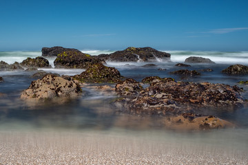 Waves crashing over rocks on the jagged coastline of Northern California, taken on a long exposure to smooth out the water and create beautiful smooth effect, against a bright blue sky
