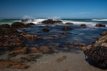 Waves crashing over rocks on the jagged coastline of Northern California, taken on a long exposure to smooth out the water and create beautiful smooth effect, against a bright blue sky