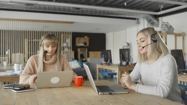 Tow woman wear headsets talking looking at laptop, female customer support manager skyping