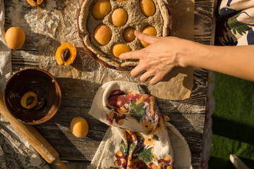 woman in gentle sundress cooking a sweet pie with fresh apricots on a sunny summer day