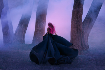 The queen in black dress, runs away in the fog. The skirt train is waving in the wind like a black...