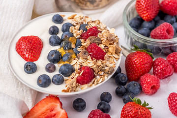 White yogurt in bowl with oatmeal and strawberries, blueberries and raspberries on the top on white background
