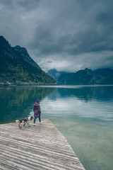 Kobieta z psem Springer Spanielem stoją na pomoście nad górskim jeziorem w pochmurny dzień	