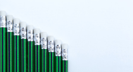 many simple pencils with erasers with green skin in a row on a white table