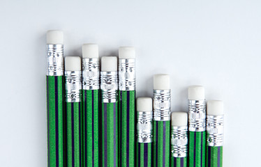 many simple pencils with erasers with green skin in a row on a white table