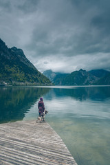 Kobieta z psem Springer Spanielem stoją na drewnianym pomoście nad górskim jeziorem Traunsee w...