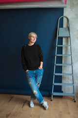 Young blonde modern woman in black sweatshirt and jeans standing near ladder (stairs) and planning renovation (repairs) 