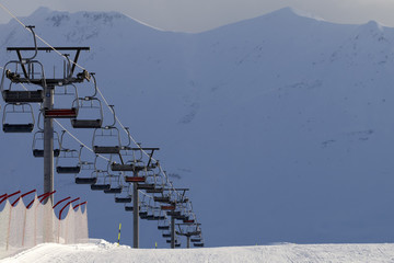 Snowy ski slope and chair lift on high mountains at winter evening