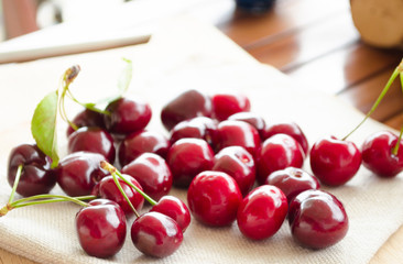 Bright juicy red berries and leaves of a sweet cherries on a linen fabric on the background of a brown wooden table. Close-up, selective focus of the image.