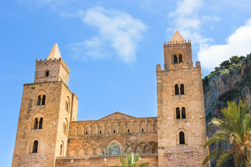 Fototapeta na wymiar Cefalu Cathedral in Sicily, Italy with blue sky and rocks behind. Famous Roman Catholic basilica erected in Norman architectural style. Part of UNESCO World Heritage and popular attraction