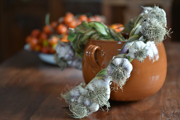 stilleben mit einem frischen knoblauchzopf, keramikschüssel und Tomaten auf einem Holztisch im Landhausstil