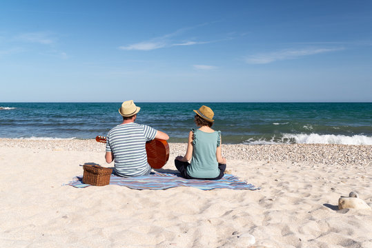 Young man playing the guitar for her friend sitting on a mediterranean beach. in a sunny day