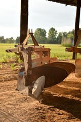 Old rusty plow sits near the edge of a field on a southern farm.
