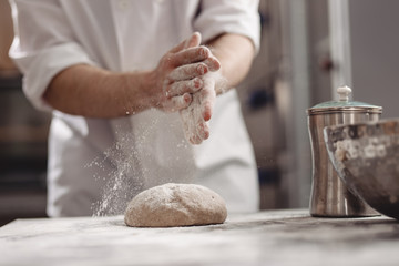 Baker adds flour to dough on the table in the bakery