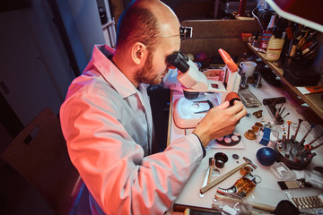 Serious watchmaker  is repairing cutomer's order at his own repairing studio.