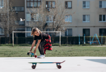 Funny boy dressed in the stylish casual clothes rides skateboard on a platform outside next to the house at the sunny warm day