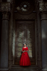 Fototapeta na wymiar Princess in a red dress stands in the palace against the backdrop of large doors.