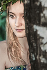 Fototapeta premium portrait of a blonde girl with a wreath of flowers in the summer near the tree