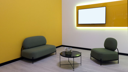Modern room in yellow style. Armchairs and a table in the corner. TV screen on the wall. Copy space and mockup.