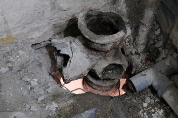 Garbage and dirt during sewage repair. Hole between the floors of an apartment building. A system of broken sanitary pipes in an old house. The concept of replacement of iron pipes for plastic.