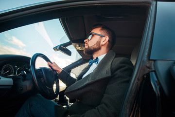 Pensive modern man in sunglasses is sitting in his car at the parking.