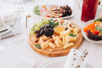 cheese plate with a bunch of grapes, honey and nuts. Gouda, parmesan, mozzarella, gorgonzola on a wooden board.