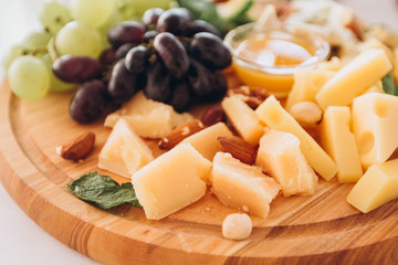 cheese plate with a bunch of grapes, honey and nuts. Gouda, parmesan, mozzarella, gorgonzola on a wooden board.
