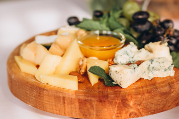cheese plate with a bunch of grapes, honey and nuts. Gouda, parmesan, mozzarella, gorgonzola on a wooden board.