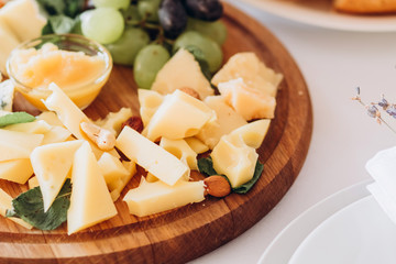 cheese plate with a bunch of grapes, honey and nuts. Gouda, parmesan, mozzarella, gorgonzola on a wooden board.