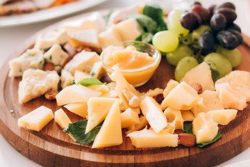 cheese plate with a bunch of grapes, honey and nuts. Gouda, parmesan, mozzarella, gorgonzola on a wooden board.