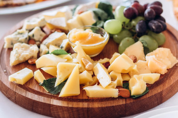 cheese plate with a bunch of grapes, honey and nuts. Gouda, parmesan, mozzarella, gorgonzola on a wooden board.
