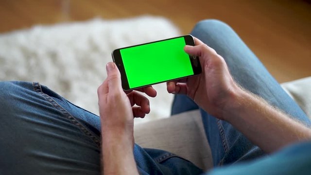 Male hands holding on a phone with a green screen horizontally and watching a video