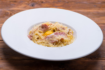 Carbonara pasta with egg yolk in a white plate on a wooden background