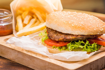 Burger with beef cutlet in a white bun on the background of french fries and tomato sauce