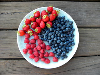 blueberries, raspberries and strawberries in a plate on a wooden table
