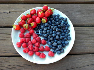 blueberries, raspberries and strawberries in a plate on a wooden table