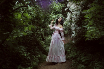 Beautiful brunette woman walks in the spring garden among lilac blossoms.
