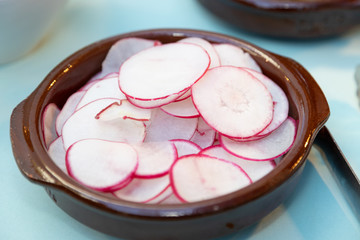 Sliced radishes served in crock bowl as condiments to tacos